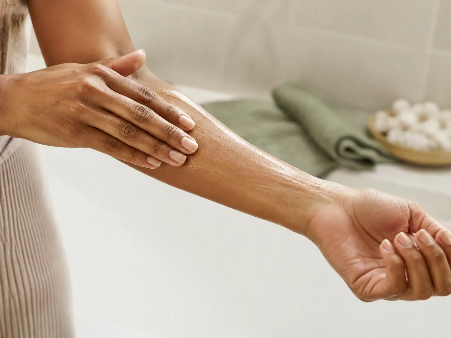 A thin layer of oil being spread over a damp forearm after showering