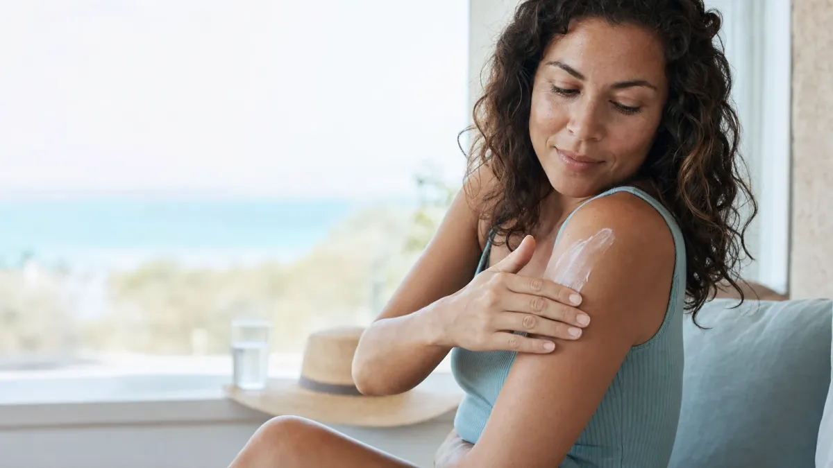 Woman applying a light moisturizer to her shoulder while resting safely in the shade after sun exposure