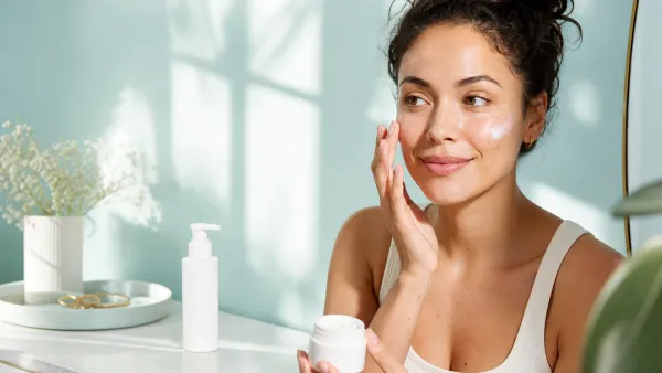 Woman applying a facial moisturizer with SPF during a bright morning skincare routine