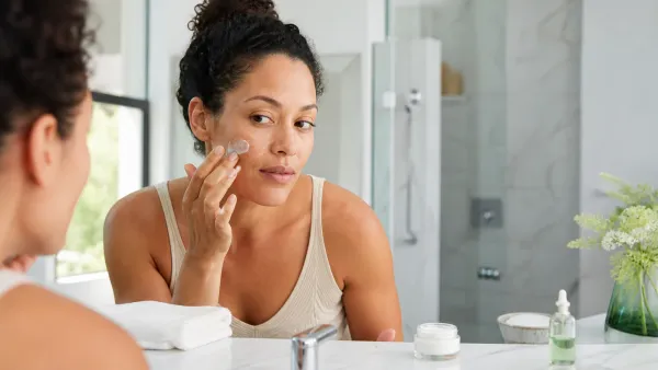 Adult applying fragrance-free moisturizer to slightly damp facial skin at a bright bathroom vanity
