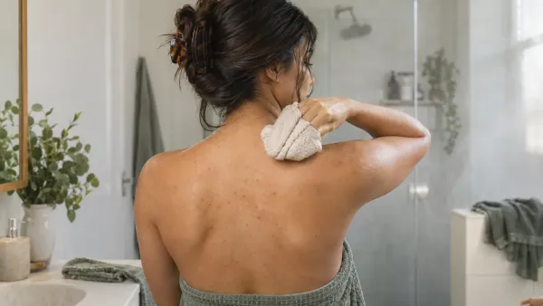 Adult with natural mild back acne gently washing the upper back in a bright bathroom